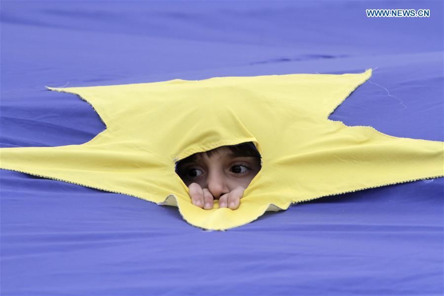 A boy looks through a cut of the European Union flag during a rally marking the 60th anniversary of the Treaty of Rome in Bucharest, Romania, on March 25, 2017. 