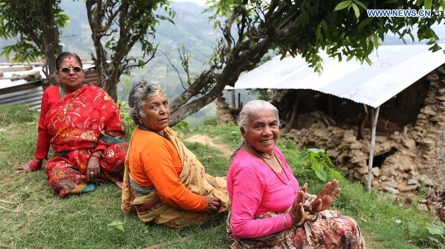 Local women sit in front of a damaged house affected by the earthquake last year at a village in Nuwakot, Nepal, June 4, 2016.