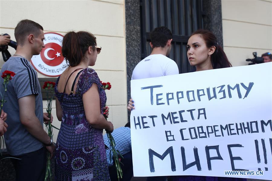 A woman stands with a placard reading 'No terrorism in a modern world' as people pass by to lay flowers in front of Turkish embassy in Russia in Moscow, Russia, on June 29, 2016. 