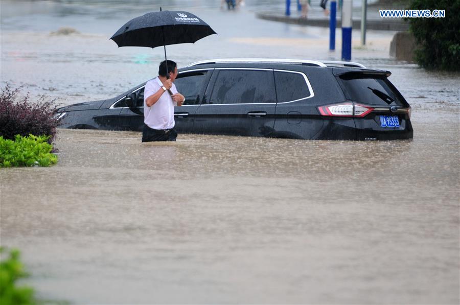 A man walks past a stranded vehicle on a flooded road in Jiujiang City, east China's Jiangxi Province, July 2, 2016. 