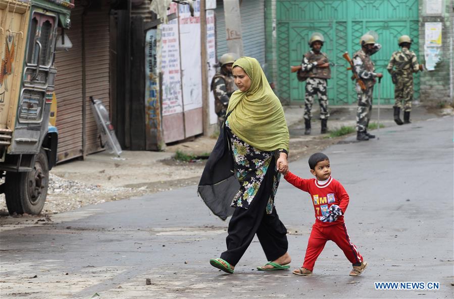 A Kashmiri woman and her child walk past Indian paramilitary troopers during the curfew in Srinagar, summer capital of Indian-controlled Kashmir, on July 18, 2016. 