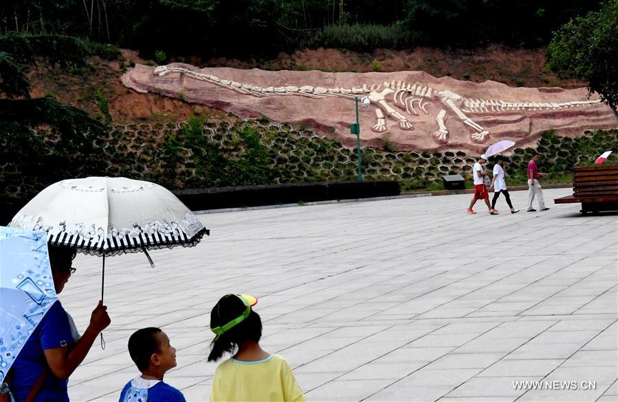 Visitors walk past a simulation dinosaur at Xixia dinosaur park in central China's Henan Province, July 25, 2016.