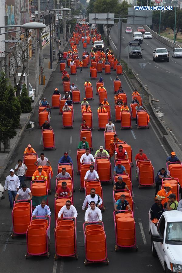 Sanitation workers walk in street after they received new trash carts in Mexico City, capital of Mexico, on March 15, 2017. 