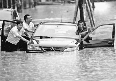 图为6月15日，市民在江西九江市濂溪区积水路段冒雨涉水前行。