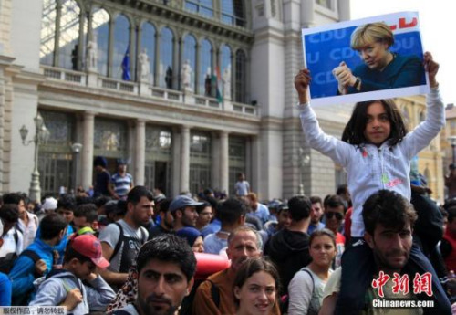 资料图：在匈牙利布达佩斯火车站，一个移民小女孩高举印有默克尔头像的招牌。