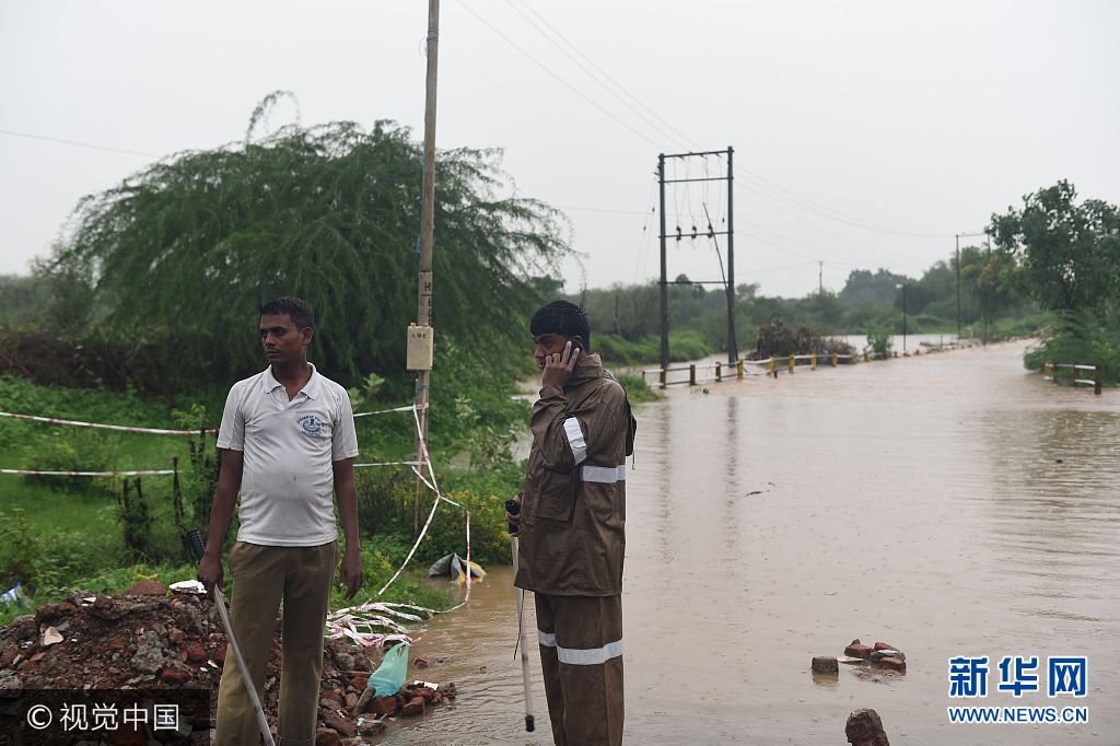 Indian police officials stand next to a submerged road covered with flood waters near Vivekanandnagar village on the outskirts of Ahmedabad on July 26, 2017. The bodies of 25 people, including 17 members of a single family, were pulled from the mud on July 26 as the death toll from major flooding in India climbed towards 120, an official said. SAM PANTHAKY