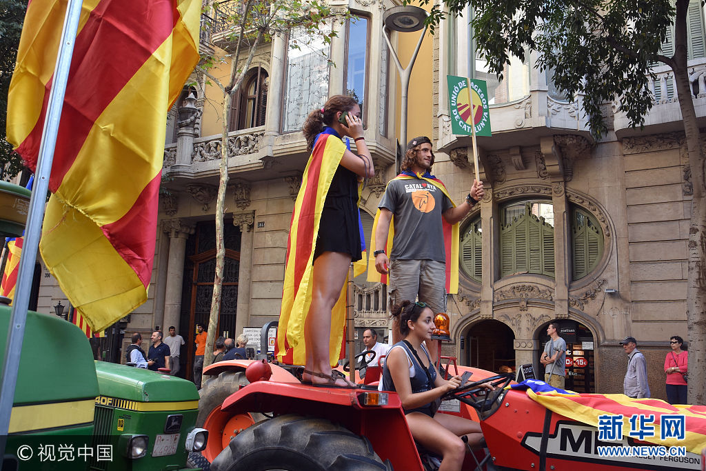 当地时间2017年9月29日，西班牙巴塞罗那，农民开拖拉机游行支持加泰罗尼亚地区独立公投。***_***BARCELONA, CATALONIA, SPAIN - 2017/09/29: A couple is seen wearing Catalonia flags on their back while standing on a tractor during a protest. Around 400 tractors called by agricultural unions have gathered on the center of the city of Barcelona to defend the referendum of the independence. (Photo by Ramon Costa/SOPA Images/LightRocket via Getty Images)